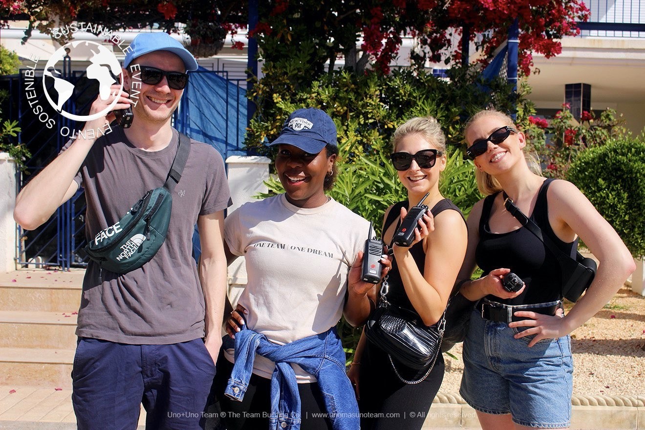 Smiling participants testing walkie-talkies at Port d'Aiguadolç in Sitges before starting En Busca del Tesoro.