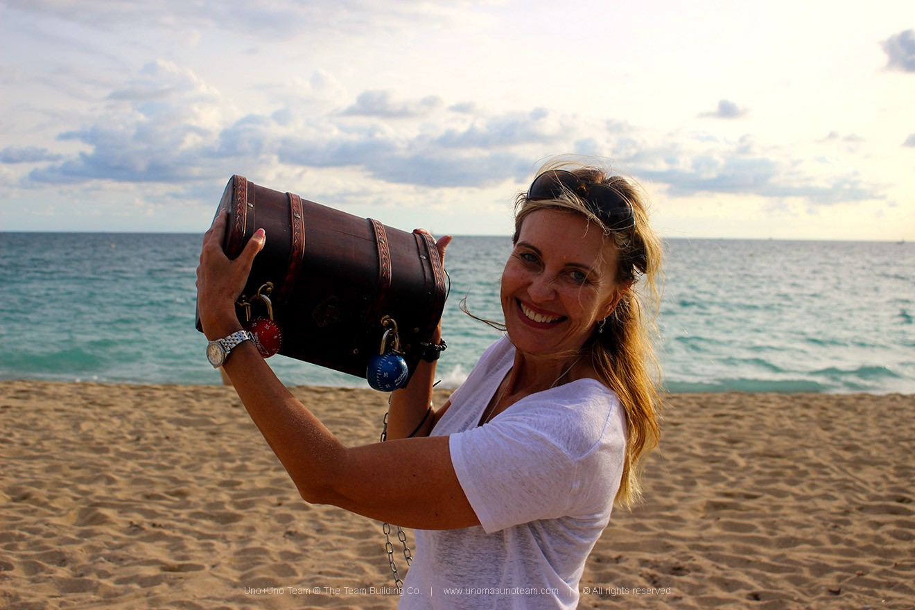 Participant raising the chest after discovering the hidden treasure at Platja de Sant Sebastià in Barcelona during the En Busca del Tesoro team building event.