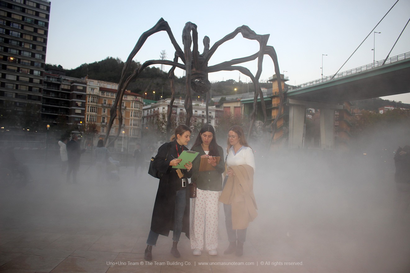 Corporate team tackling a problem-solving challenge surrounded by mist near the 'Maman' sculpture and the Guggenheim Museum in Bilbao during En Busca del Tesoro.