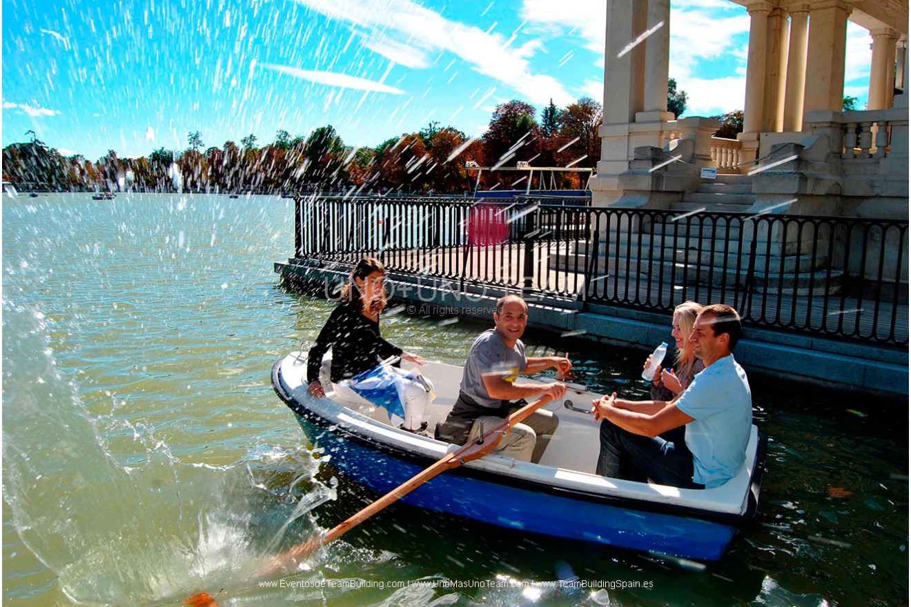 Four participants navigating a rowing boat in front of the Alfonso XII Monument on El Retiro Park Lake during En Busca del Tesoro in Madrid